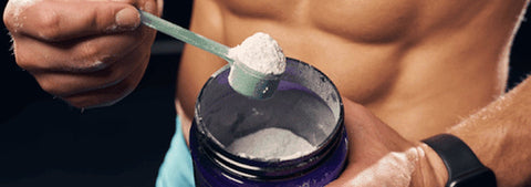 Athlete scooping creatine powder into a shaker bottle.